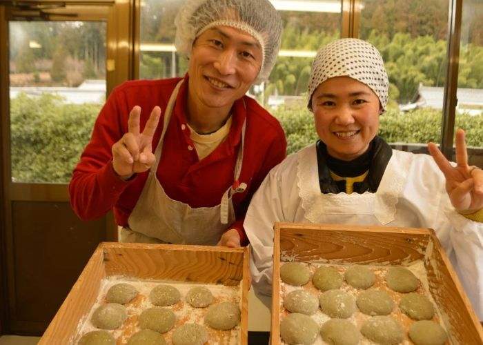 Two people at a washi paper and mochi-making class giving peace signs to the camera while showing off their mochi.